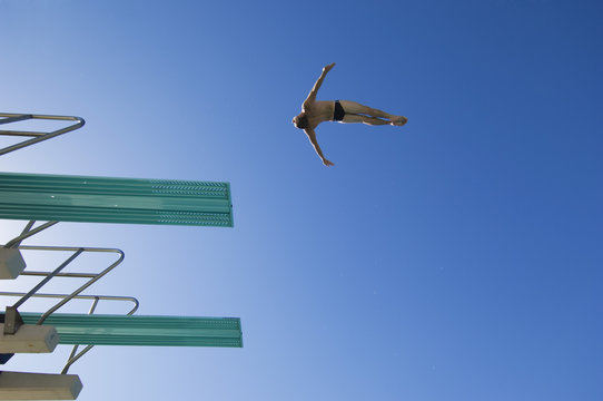 Low angle view of a male swimmer preparing to dive from diving board against clear blue sky