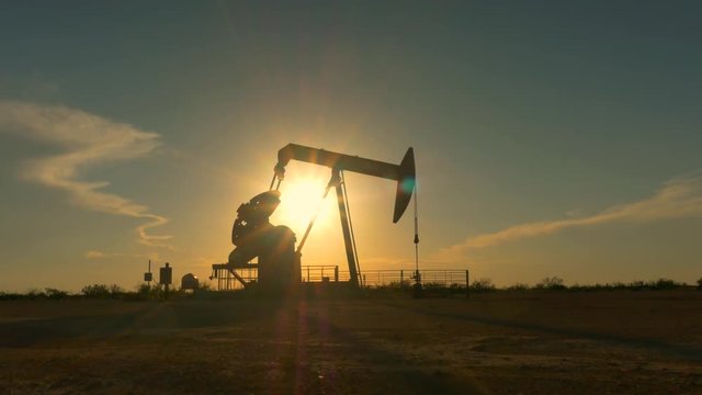 Industrial jack pump platform pumping crude oil over sunset sun