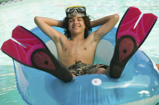 Full length of happy boy relaxing on inflatable tube in swimming pool at resort - Powered by Adobe