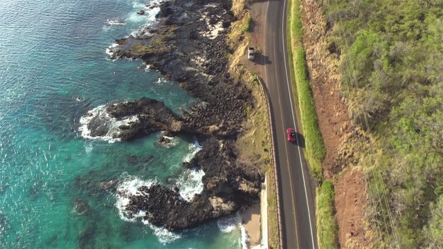 AERIAL: Red convertible driving on amazing coastal road above rocky ocean cliffs