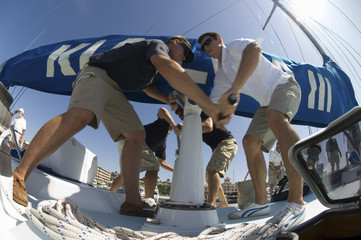 Low angle view of crew members operating windlass on yacht