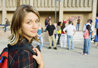 Portrait of beautiful young woman on college campus with classmates in background