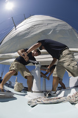 Low angle view of crew members operating windlass on yacht