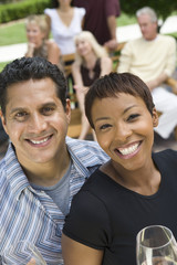 Portrait of happy couple holding glasses of wine with friends in background