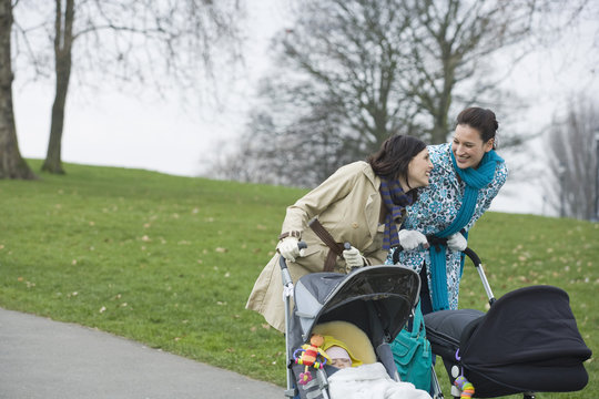 Cheerful young mothers pushing strollers in park