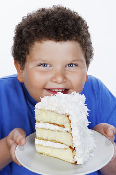 Closeup portrait of a smiling overweight boy holding large slice of cake