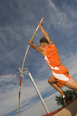 Low angle view of a male athlete performing a pole vault against the sky