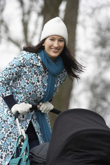 Portrait of happy young mother walking with baby carriage in park