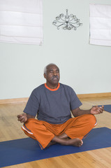 An African American senior man meditating in lotus position - obrazy, fototapety, plakaty
