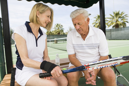 Senior Caucasian couple relaxing on bench after playing tennis