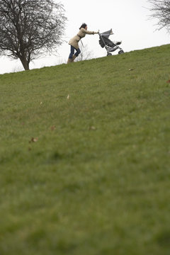 Young Mother Pushing Stroller Uphill In Park