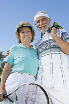 Portrait of happy senior couple holding tennis racquet and balls against clear sky