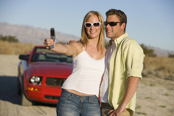 Couple taking self portrait through mobile phone with car in the background