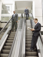 Low angle view of multi ethnic businessmen standing on escalator in office