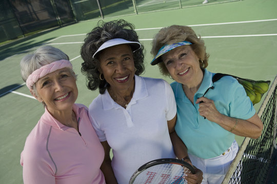 Three female senior tennis players in court smiling