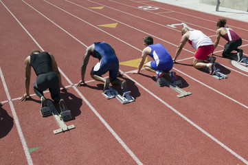 Rear view of multiethnic runners preparing for race at starting blocks