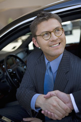 Happy middle aged businessman sitting in car and shaking hands with his colleague