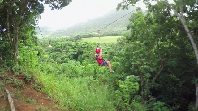 Young woman speed traveling on a zipline rope high above fascinating deciduous overgrown tropic jungle canopies. Adrenaline high speed slope gravity travelling on a rope from top to bottom