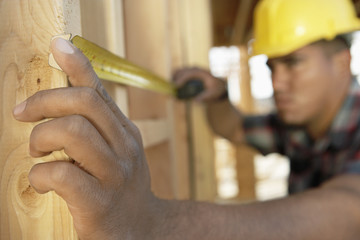 Closeup of a construction worker measuring between boards with tape measure at construction site
