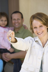 Portrait of happy woman holding new home key with family in background