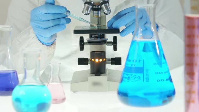researcher analysing a sample with a microscope, ampoule and technical equipment