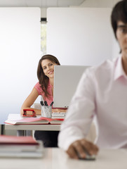 Portrait of smiling businesswoman using computer with male colleague in foreground