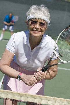 Happy senior woman playing tennis in court