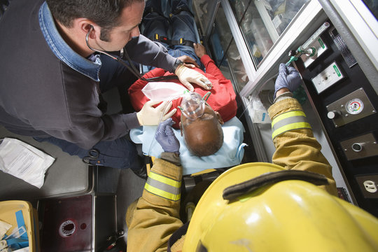 Male firefighter and EMT doctor taking care of an injured senior man in ambulance