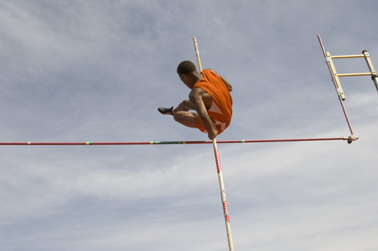 Low angle view of male pole vaulter clearing bar against cloudy sky