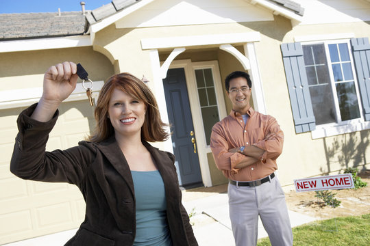 Portrait of happy woman holding keys of new home with man standing in background