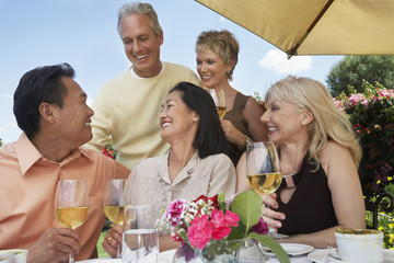 Group of multiethnic friends enjoying drinks at dinner table outdoors