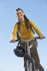 Fototapeta na wymiar Portrait of a smiling young woman riding mountain bike against the clear blue sky