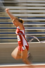 Blurred motion of excited female athlete runner crossing the finishing line with arms raised