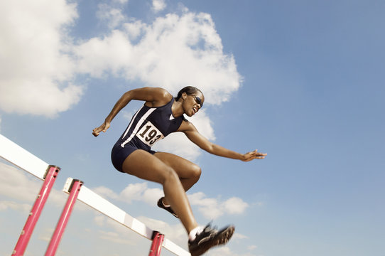Low angle view of a female athlete jumping hurdle