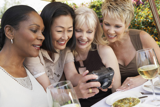 Happy multiethnic female friends looking at photos on digital camera at garden party