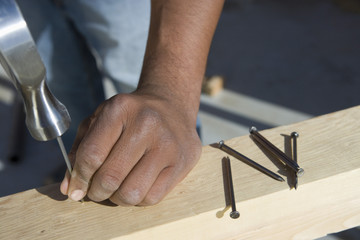 Extreme closeup of hand hammering nail to the plank