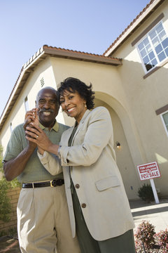 Portrait of happy senior couple holding key in front of new house