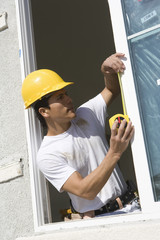 Male foreman taking measure of window with measure tape at construction site