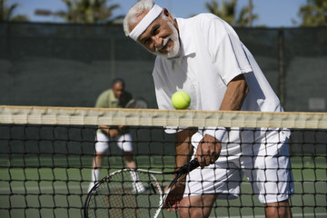 Happy senior man playing doubles on tennis court