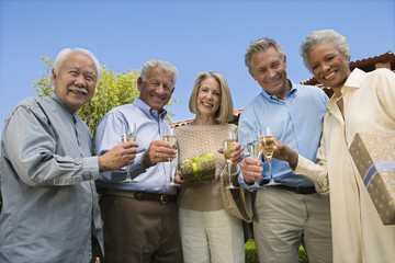 Low angle view of multiethnic senior friends standing together with champagne glass at lawn