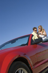 Low angle view of couple sitting on car with handycam against clear sky