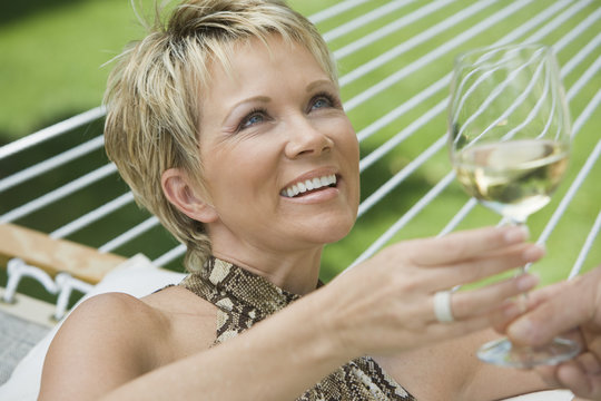 Happy Mature Woman With Man Holding Wine Glass On Hammock