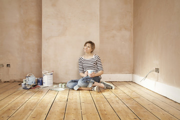 Thoughtful woman holding coffee mug sitting on floorboard