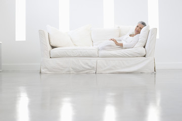 Fototapeta premium Full length portrait of senior woman sitting on sofa in spacious room