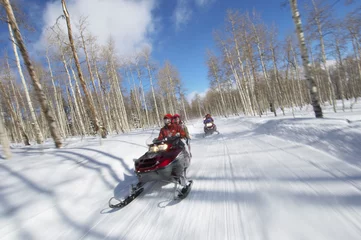 Fotobehang Two couples riding on two snowmobiles along the snowy track © moodboard