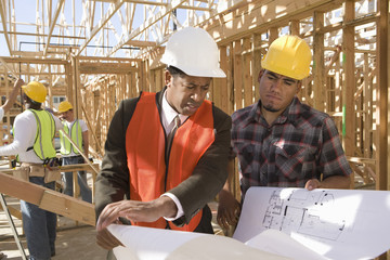 Architect and foreman having discussion over blueprint with workers in background at construction site