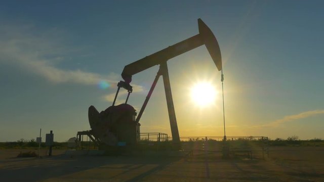 Industrial jack pump platform pumping crude oil over sunset sun