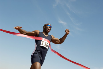 Low angle view of an African American male runner winning race against blue sky