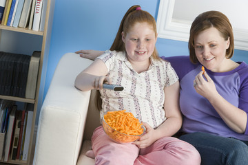 Happy mother and daughter watching television at home