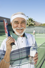 Portrait of a happy senior male tennis player holding water bottle at court